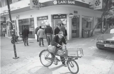  ?? SIMON DAWSON / BLOOMBERG NEWS ?? A man pushes his bicycle past a queue of people waiting to withdraw cash from automated teller machines in Cyprus after the government proposed taxing bank accounts. Columnist Jason Heath says Canadians
shouldn’t turn away from investing and banks.