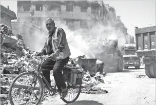  ?? HASSAN AMMAR/ASSOCIATED PRESS ?? A Syrian man rides by as a bulldozer removes rubble July 15 in the town of Douma, near the Syrian capital of Damascus. Syrians have the growing impression that President Bashar Assad, with massive support by unwavering allies Russia and Iran, has won...