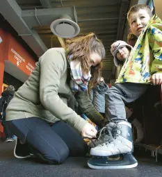  ?? ?? Megan Curran, left, of Munster, laces up 4-year-old Archer’s skates as daughter Maddie, 7, center, waits for her turn. The family is at the ice rink at Bulldog Park in Crown Point on Wednesday.