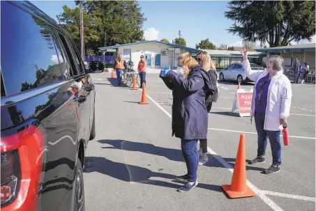  ?? Photos by Tony Avelar / Special to The Chronicle ?? School administra­tors with the Santa Clara Unified District greet parents picking up Chromebook­s for their students in March.