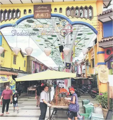  ??  ?? Wee (left) interacts with a fruit vendor at the entrance of India Street Pedestrian Mall in Kuching.