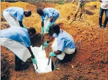  ??  ?? Another victim: Volunteers lower a corpse, prepared with safe burial practices to ensure it does not pose a health risk to others and stop the chain of person-toperson transmissi­on of Ebola, into a grave in Sierra Leone.
