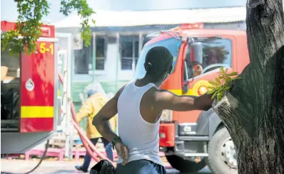  ?? FILE ?? In this September 17, 2021 Gleaner photo, a man looks on from the shade as firefighte­rs from the Jamaica Fire Brigade work to contain a fire in Kingston.