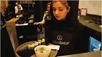  ??  ?? A waitress takes a plate of sushi from the kitchen.