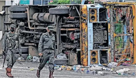  ?? | AFP ?? SECURITY personnel walk past a burned vehicle along a road after they were torched by protesters in Colombo, yesterday amid protests over the country’s economic crisis.