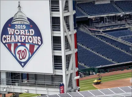  ?? ANDREW HARNIK — ASSOCIATED PRESS ?? A large 2019 World Champions banner hangs from the back of the centerfiel­d scoreboard at Nationals Stadium in Washington, D.C., as workers water the infield Wednesday.