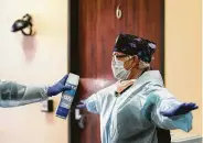  ??  ?? Registered nurse Krista Rozell is sprayed down with disinfecta­nt after completing a preliminar­y exam of a patient at Texas Emergency Care Center.