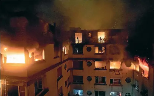  ?? AP ?? A fire rages through the top floors of an apartment building in Paris, France. The fire that authoritie­s suspect was an arson attack sent residents fleeing to the roof or climbing out their windows to escape.