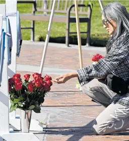  ?? ?? A mourner touches roses in front of wooden hearts carrying messages at a makeshift memorial. Above, people write messages on the hearts, outside Monterey Park City Hall.