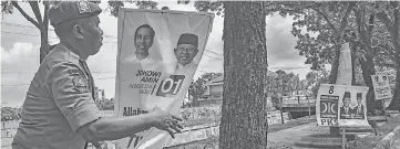  ?? — AFP photo ?? A member of Indonesia’s Public Order Service (Satpol PP) takes down election campaign banners in Pekanbaru following the end of the campaignin­g period ahead of the April 17 polls.