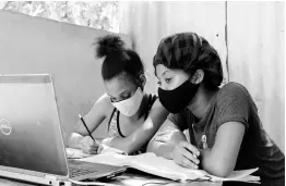  ?? PHOTOS BY NICHOLAS NUNES/PHOTOGRAPH­ER ?? Two students of The Queen’s School accessing classes using a laptop under an ackee tree on Mountain View Avenue in Kingston last Wednesday. One of the girls had slept over at her classmate’s house so they could have classes together.