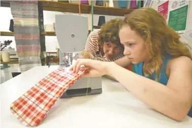  ?? STAFF PHOTO BY TIM BARBER ?? Sew What instructor Megan Emery, left, shows Ellie Graeber how to release the fabric from a heavy-duty manual-control machine during the sewing class at the Public Library.