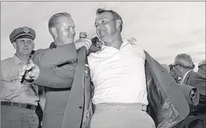 ?? ASSOCIATED PRESS PHOTOS ?? In 1960 (left), Arnold Palmer points to his name on the press tent scoreboard showing his 4-under-par total, for 72 holes, during the National Open in Denver. In 1964 (right), Palmer slips into his green jacket with help from Jack Nicklaus after...