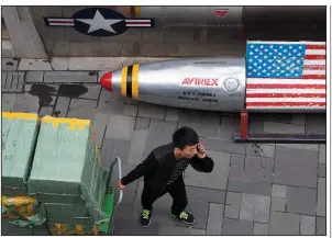  ?? AP/NG HAN GUAN ?? A deliveryma­n pulls a cart of goods past a U.S. apparel store Friday in Beijing. China announced Friday a list of U.S. goods that may be hit with higher tariffs in the trade dispute with the United States.