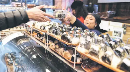  ?? ?? A customer (left) buying a rice ball, known as ‘onigiri’, at an Omusubi Gonbei shop in the Manhattan borough of New York.