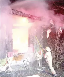  ?? Keith Bryant/The Weekly Vista ?? Bella Vista deputy fire chief Bryan Wolfgang rips paneling from the burning home on Ciemny Lane Tuesday, Dec. 6, so the deck gun’s water can better reach the flames.