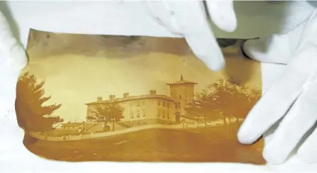  ?? CLIFFORD SKARSTEDT/EXAMINER ?? Conservato­r Basia Baklinski with photograph­s of the Union School, later Central Public School and now an apartment building (with the central tower removed) from a time capsule on Aug. 19. The time capsule was buried in 1864 and was found by Shawn...