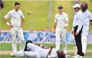  ?? — AFP ?? Umpire Rod Tucker with New Zealand’s Trent Boult (left) look at West Indies’ Miguel Cummins as he lies on the ground after being hit on the knee by the ball during day four of the first Test.