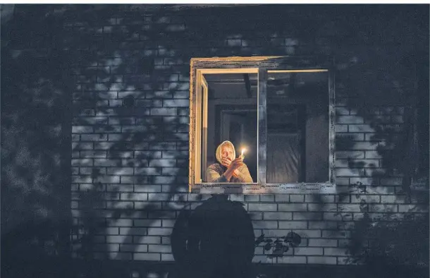  ?? FOTO: EMILIO MORENATTI/AP ?? Die 70-jährige Catherine schaut mit einer Kerze in der Hand aus ihrem Fenster in Borodjanka in der Region Kiew.
