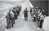  ?? DARIO LOPEZ-MILLS AP ?? A group of migrants stand next to the border wall as a Border Patrol agent takes a head count in Eagle Pass, Texas, in May.