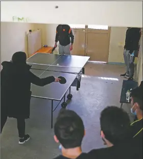  ??  ?? A teacher plays table tennis with an inmate as others watch them.