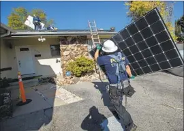  ?? Mel Melcon Los Angeles Times ?? INSTALLER Luis Jimenez of Sunrun carries a panel at a Granada Hills home this month. Rooftop solar is a cost-effective climate solution, researcher­s say.