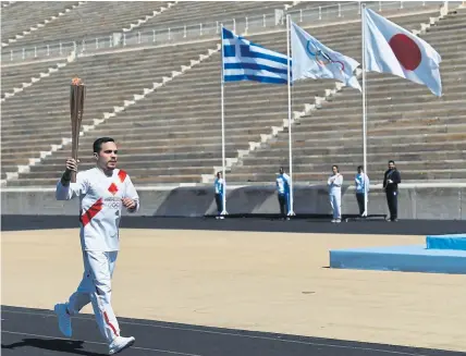  ??  ?? An athlete carries the Olympic torch during the Flame Handover Ceremony for the Tokyo Olympics on Thursday in Athens. The ceremony was held behind closed doors as a preventive measure against the coronaviru­s outbreak.