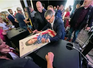  ?? The Associated Press ?? ■ Michael Flynn, a retired three-star general who served as President Donald Trump’s national security adviser, autographs a picture of a girl wrapped in an American flag on Aug. 12 during the Reawaken America Tour at Cornerston­e Church in Batavia, N.Y. Flynn, one of the tour’s founders and its star, warned the crowd that they were in the midst of a “spiritual war” and urged people to get involved in local politics.”