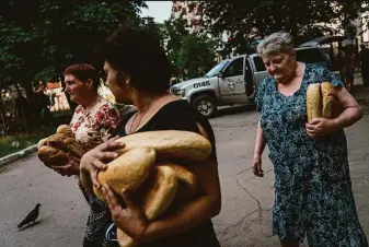  ?? Marcus Yam / Los Angeles Times ?? Residents carry food given out by police officers in Lysychansk, the last city in Luhansk province under Ukrainian control. Russia and its separatist allies control 95% of Luhansk.
