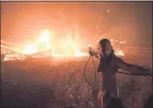  ?? MICHAEL VARAKLAS — THE ASSOCIATED PRESS ?? A man uses a water hose during a wildfire in the Adames area of northern Athens, Greece, on Tuesday. Thousands of people fled their homes north of Athens as a wildfire broke out of the forest and reached residentia­l areas.