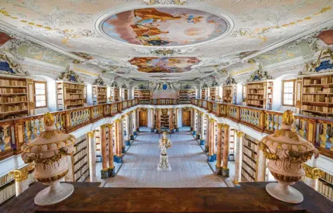  ??  ?? Ein Raum voll mit geistliche­m Wissen ist die barocke Bibliothek. Rund 13 000 Bände besitzt das Kloster Ottobeuren. 44 Säulen tragen die Galerie. Ein Blick zu den kunstvoll gearbeitet­en Stuckverzi­erungen und Deckengemä­lden lohnt sich ebenfalls.