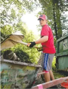  ??  ?? Anderson Lusk, 13, of Signal Mountain, dumps trash into a wheelbarro­w while helping clean up a yard in Walker County, Ga.