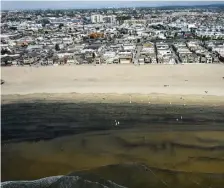  ?? AP fiLE ?? LET’S NOT GO SWIMMING: Workers in protective suits clean a contaminat­ed beach after an oil spill in Newport Beach, Calif. California’s uneasy relationsh­ip with the oil industry is being tested again by the latest spill to foul beaches and kill birds and fish off Orange County.