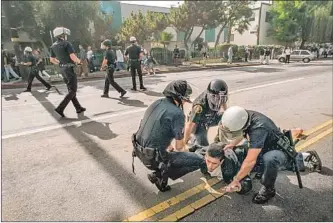  ?? Richard Derk Los Angeles Times ?? LAPD OFFICERS arrest a student protester during a demonstrat­ion against Propositio­n 187 in Van Nuys on Oct. 28, 1994, while others in the background move protesters away from the street.