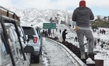  ?? GETTY IMAGES ?? Cars are lined up after people parked on the side of the freeway to walk and play in the snow along Highway 14 in Los Angeles County on Sunday near Acton, Calif., where a major storm carried a rare blizzard warning.