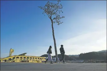  ??  ?? A man and a woman walk near a replica of a lone pine tree that initially survived the 2011 tsunami that flattened the surroundin­g coastal forest in Rikuzentak­ata, Japan. The tree, which eventually died of seawater exposure, was known as the “Miracle Pine,” and townspeopl­e treated, reinforced and then preserved it as a memorial and symbol of hope for the region.