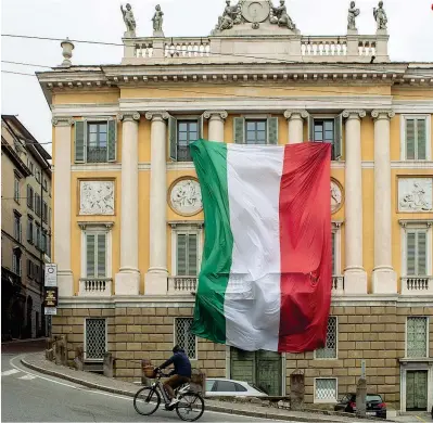  ?? (Getty Images) ?? A Bergamo Una persona in bicicletta davanti a Palazzo Medolago Albani, sul Viale delle Mura, che espone il Tricolore