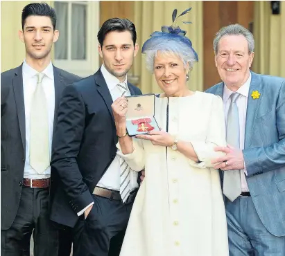  ?? Picture: KATE GREEN/ALPHA/REX ?? Lynda receiving her OBE in 2014, with her sons, Michael and Robert, and third husband Michael Pattemore