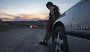  ??  ?? A woman who was evacuated from Cache Creek rests on the front of her car along the Trans-Canada Highway in Savona, as smoke from a wildfire burning near Ashcroft rises in the distant sunset.