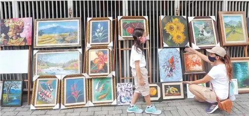  ?? BOY SLAMET/JAWA POS ?? BURSA KARYA SENI: Syska La Veggie dan anaknya, Afika Dara, melihat lukisan-lukisan yang dipamerkan di trotoar Jalan Ponti kemarin.