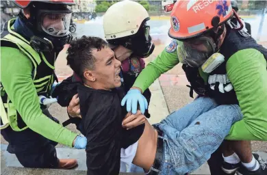  ?? AFP/GETTY IMAGES ?? An anti-government activist is assisted Sunday by medics during clashes with the police that erupted during a protest against the elections for a Constituen­t Assembly in Caracas. Troops fired weapons to clear protesters in Caracas and elsewhere.