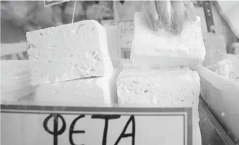  ?? ARIS MESSINIS / AFP / GETTY IMAGES ?? A shop assistant lifts a slab of feta cheese at a shop in Athens. Greece wants exclusive rights to the name feta for the cheese in Canada.