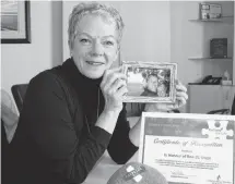  ?? KATHERINE HUNT/SALTWIRE NETWORK ?? Wendy Toy holds a photo of her with her late husband Ron St. Onge who was an avid blood donor. Next to her is the bandage from her first time giving blood and a certificat­e from Canadian Blood Services for the blood clinic held each year in honour of St. Onge. This year’s clinic in memory of St. Onge is being held today.