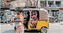  ?? ?? A STREET trader walks past a motorised rickshaw in Lagos. Nigeria’s central bank is turning to the nation’s three-wheeler taxi operators to speed the adoption of the enaira, say the writers. | Bloomberg