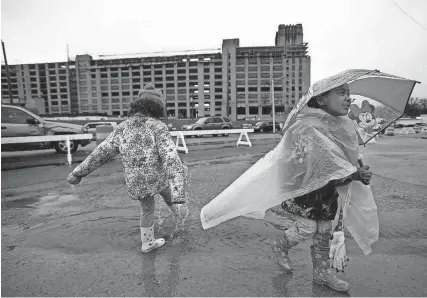  ?? THE COMMERCIAL APPEAL FILES ?? Feb. 21, 2015: From right, Ava and Ellie Sheehan play in puddles in front of the Sears Crosstown building during a break in the rain at the groundbrea­king party to commemorat­e the constructi­on on the Sears building, which began Jan. 1. The building has been renamed Crosstown Concourse.