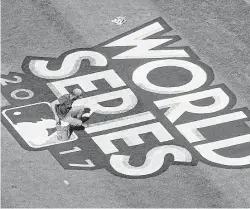  ?? Karen Warren / Houston Chronicle ?? Dodgers groundskee­pers paint the World Series logo on the field during media day at Dodger Stadium on Monday. It’s shaping up to be a hot day for the opening game at Chavez Ravine with the high expected to be 100.