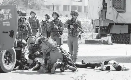  ?? Hazem Bader
AFP/Getty Images ?? ISRAELI TROOPS tend to an injured soldier lying near the body of a Palestinia­n man who stabbed him near the entrance to Hebron in the West Bank, near the Israeli settlement of Kiryat Arba. The Israeli military said that the man was disguised as a news...