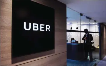  ?? ANTHONY WALLACE/AFP ?? An employee stands near an Uber sign at the entrance of the ride-hailing giant’s office in Hong Kong on March 10.