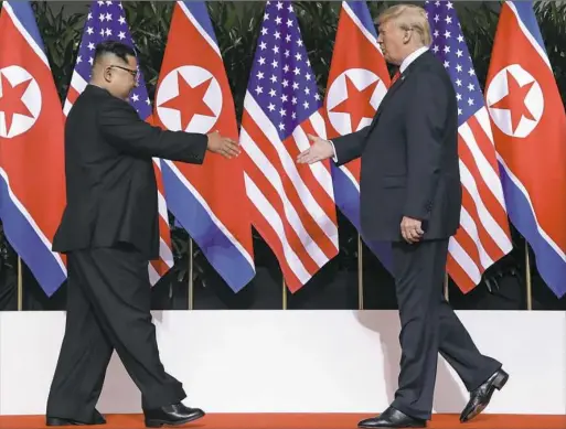  ?? Evan Vucci/Associated Press ?? U.S. President Donald Trump and North Korea leader Kim Jong Un reach to shake hands at the Capella resort on Sentosa Island Tuesday in Singapore.