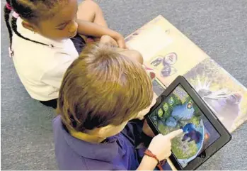  ?? TAIMY ALVAREZ/STAFF PHOTOGRAPH­ER ?? Kindergart­ner Adrian Erazo, 6, shows first-grader Kaylee Sabrina Barker, 6, how to use the book Animal Kingdom.